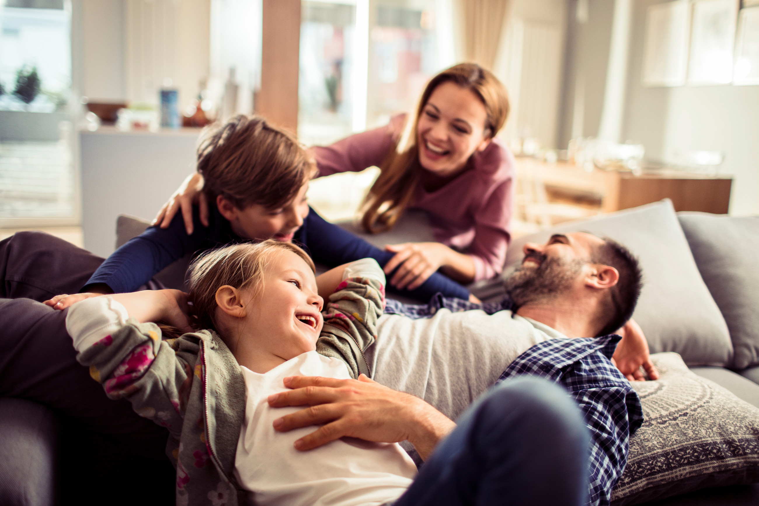 A family snuggled on a couch, smiling with double glazed windows in the background