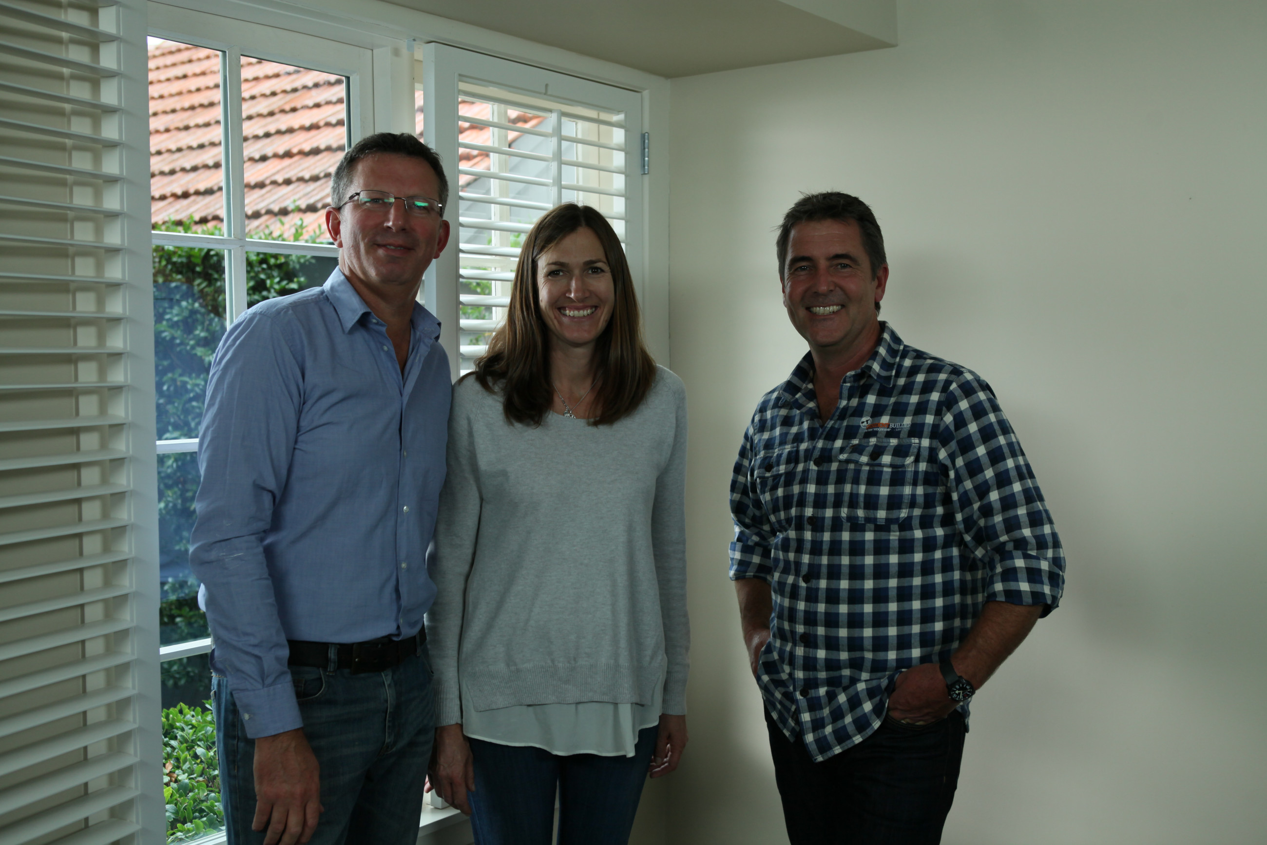 Three people smiling in their home in front of double glazed windows