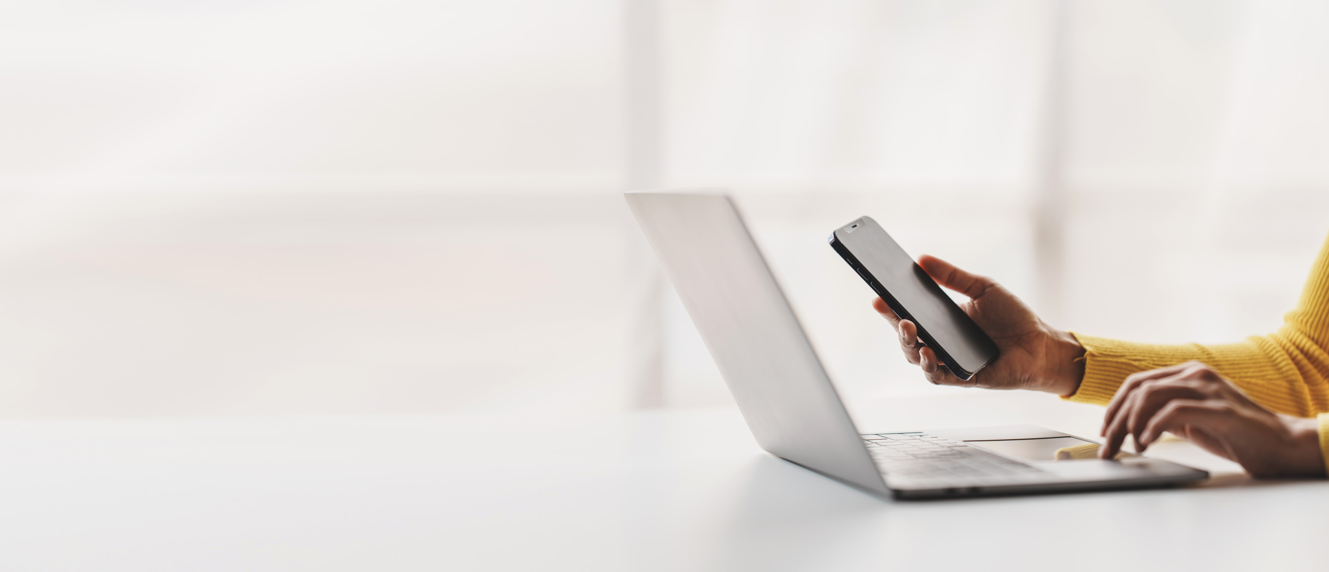 A woman multitasking on her phone and laptop, sitting near double glazed windows